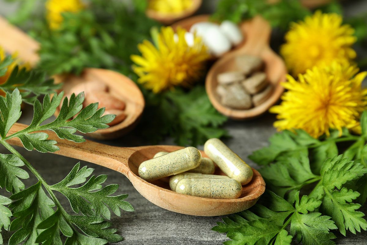 Pflanzliche Kapseln und Tabletten auf Holzlöffeln, umgeben von Heilkräutern – Phytotherapie